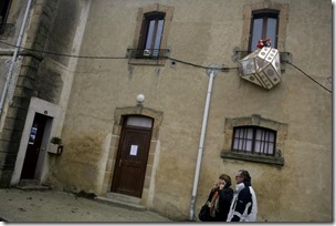 People walk past a model meant to represent a UFO hanging outside a window in Bugarach